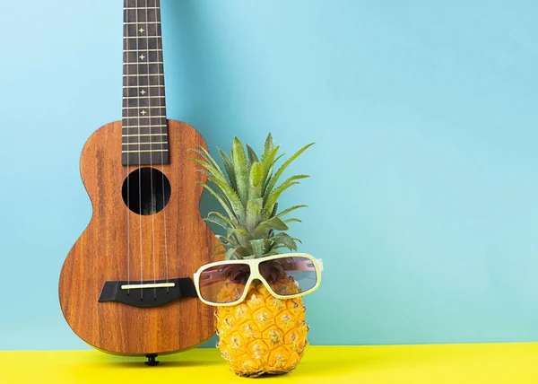 Funny pineapple with glasses, guitar on a bright blue background. Recreation and summer party concept. Horizontal frame.