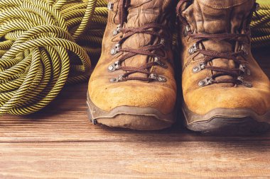 Bir çift kahverengi yıpranmış botları ve ahşap arka plan üzerinde bir spor ip. Seçici odak. Kavramı seyahat ve macera.