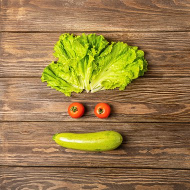 Ahşap bir arka plan üzerinde taze sebze domates kabak marul ile Eğlenceli komik yüz. Sağlıklı gıda vejetaryenlik.