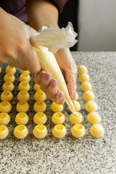 Cooking handmade chocolates. A confectioner pours liquid white chocolate into molds. Close-up. Selective focus.