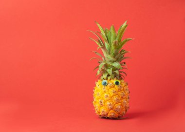 Kırmızı parlak arka planda gözleri olan olgun ananas. Tropik bir meyvenin komik namlusu. Kavram Yatay çerçeve.
