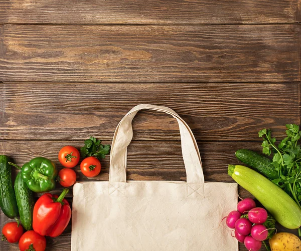 Cotton shopping bag and fresh rustic vegetables on a wooden background. Eco Concept. Copy space. Flat layout.