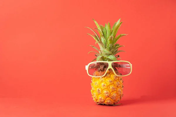 Желтый спелый ананас в темных солнечных очках на красном фоне. Забавное лицо из тропических фруктов. Концепция копирования пространства . — стоковое фото