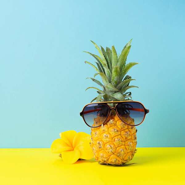 Yellow ripe pineapple in sunglasses on a yellow blue background. Funny face from a tropical fruit. Concept