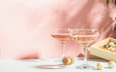 Şampanya rengi veya şarap gözlük, pembe arka plan parlak ışık beyaz ve koyu çikolata şekerkutusu. Kopyalama alanı.