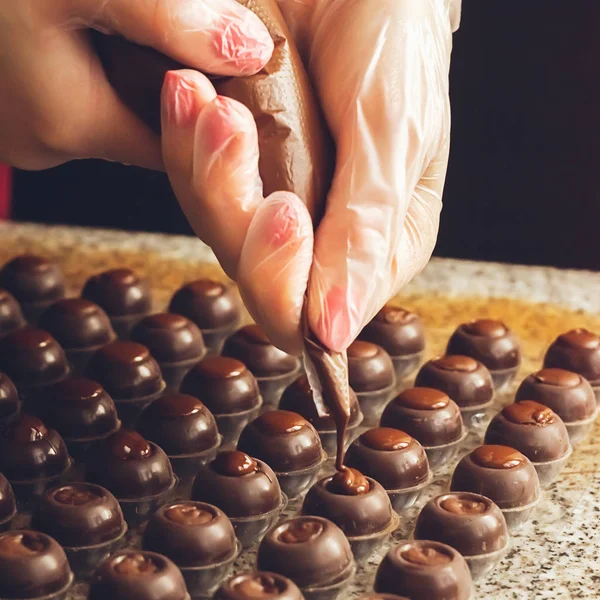 Making handmade chocolates. A confectioner pours liquid dark chocolate into molds. Close-up. Selective focus. Square