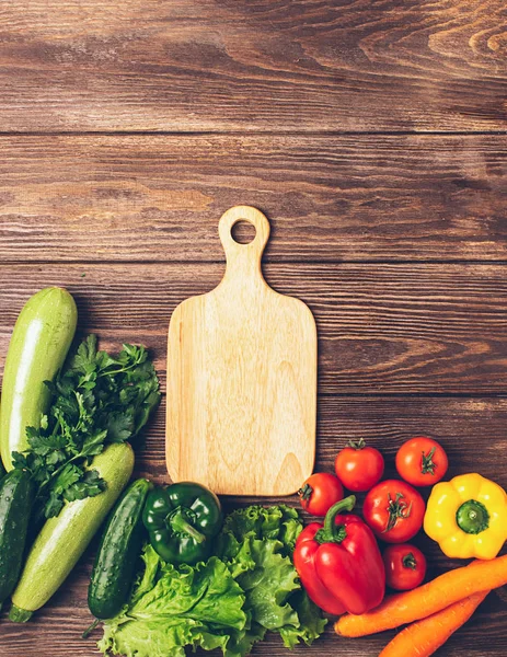 Verduras frescas de diferentes colores tabla de cortar fondo de madera. Vegetarianismo y nutrición saludable. Diseño plano . — Foto de Stock