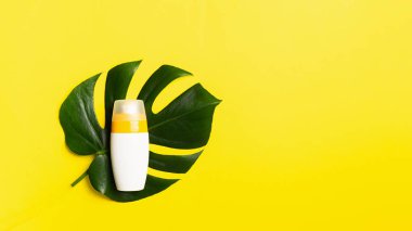 Parlak sarı bir arka plan üzerinde tropikal bitkilerin bir şişe büyük levha güneş kremi. Yaz tatili konsepti ve plaj.