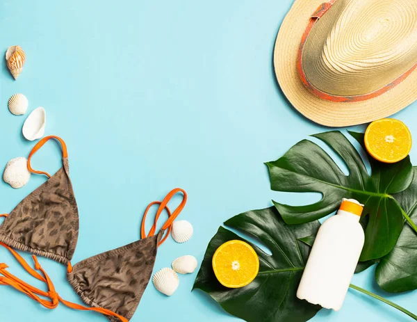 Verano accesorios de playa sombrero traje de baño protector solar hojas de planta tropical de fondo azul brillante. El concepto de la playa . —  Fotos de Stock