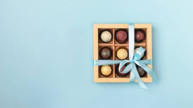 Parlak mavi bir arka plan üzerinde bir sadan mavi kurdele ile kağıt kutusu işçiliği çeşitli çikolatalar. Düz yatıyordu. Kopyalama alanı