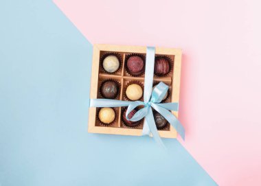 Parlak renkli bir arka plan üzerinde bir sadan mavi kurdele ile kağıt kutusu işçiliği çeşitli çikolatalar. Düz döşeme konsepti.