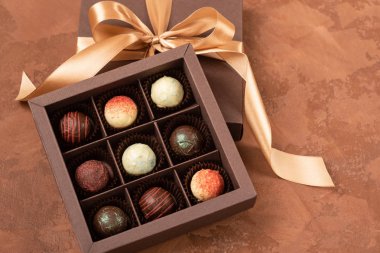 Kahverengi dokulu arka plan üzerinde sadan kurdele ile koyu bir kağıt kutusunda Çikolata şekerler. Düz yatıyordu. Şenlikli konsept.