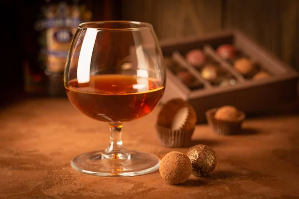 Een glas sterke alcoholische drank brandewijn of brandewijn en een doos chocolaatjes op een donkere achtergrond. Selectieve focus. — Stockfoto