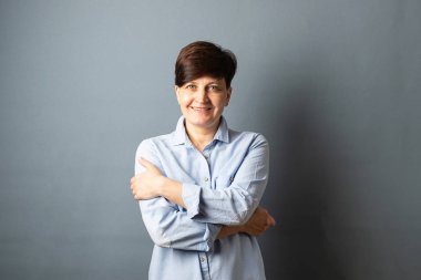 Orta yaşlı bir kadın duvarın yanında poz lar. Gri arka planda kadın portresi. Kopyalama alanı.