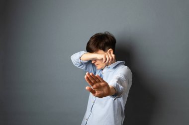 Bir kadın elleriyle yüzünü ve başını kapatır, saklanır. Gri arka planda kadın portresi. Kopyalama alanı.