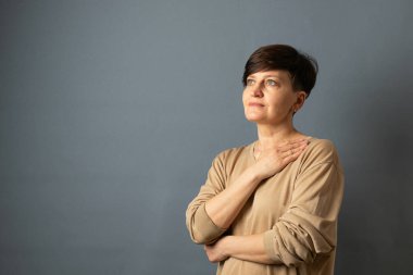 Orta yaşlı bir kadın duvarın yanında poz lar. Gri arka planda kadın portresi. Kopyalama alanı.