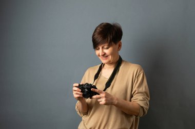 Bir kadın bir kamera tutar ve fotoğraflara bakar. Gri arka planda kadın portresi. Kopyalama alanı.