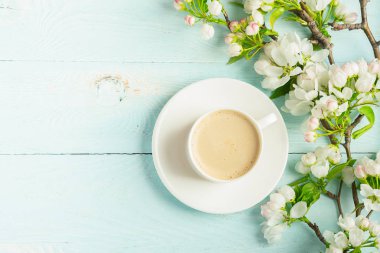 Sıcak aromatik kahve bir fincan ve ahşap mavi arka plan üzerinde bir elma ağacının çiçek açan bir dalı. Düz düzen.