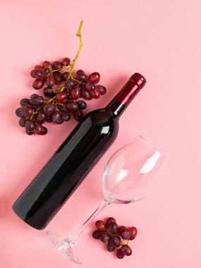 Bir şişe şarap, yumuşak pembe bir arka plan üzerinde bir demet üzüm. Minimalizm. Üstte görüntü