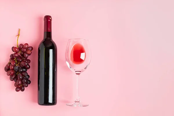 Bir şişe şarap, yumuşak pembe bir arka plan üzerinde bir demet üzüm. Minimalizm. Üst görünüm düz düzen. — Stok fotoğraf