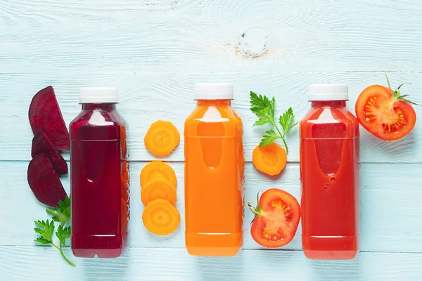 Zumo fresco batidos de una variedad de verduras zanahorias tomates manzana remolacha en botellas sobre un fondo azul de madera . — Foto de Stock