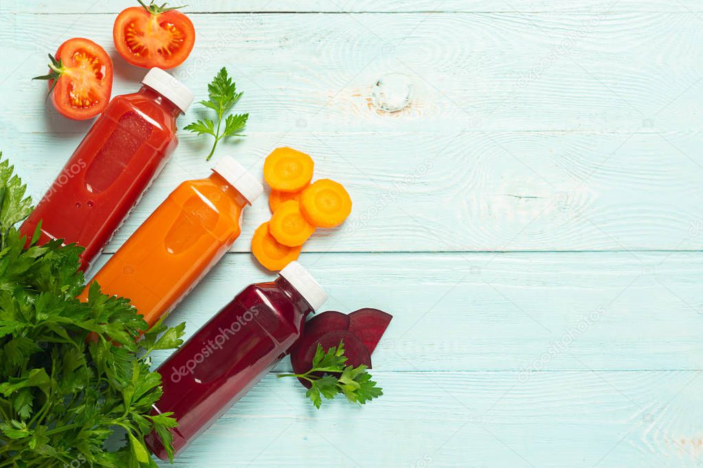Fresh juice smoothies from a variety of vegetables carrots apple tomatoes beets in bottles on a wooden blue background.