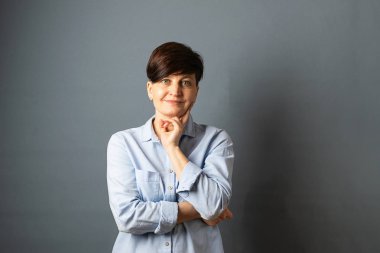 Gri boş arka planda kısa saç kesimi olan genç bir kadının portresi. İnsan duyguları yüz ifadesi mutluluk sevinç.