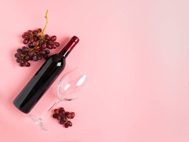 Bir şişe şarap, yumuşak pembe bir arka plan üzerinde bir demet kırmızı üzüm den oluşan boş bir bardak. Düz düzen üst görünümü. Kopyalama alanı.