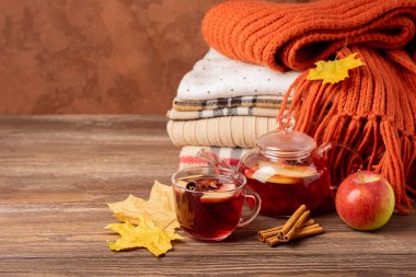 İçecek bir cam fincan ve su ısıtıcısı ve ahşap bir arka plan üzerinde örme giysi yığını sonbahar elma kırmızı çilek. Sıcak çay.
