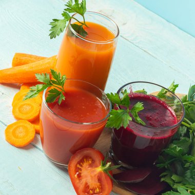 Ahşap mavi arka plan üzerinde gözlük sebze pancar elma havuç domates çeşitli taze meyve suyu smoothies.