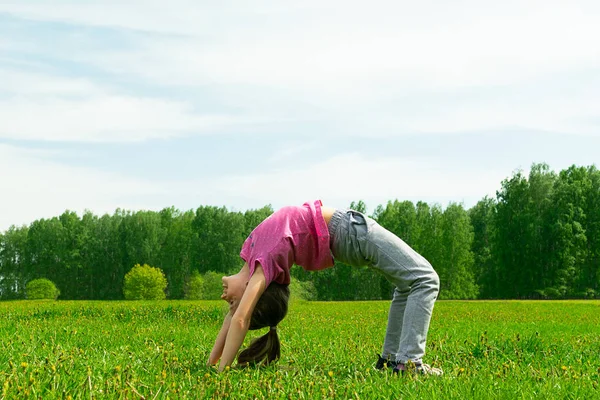 La niña hace gimnasia de yoga en un prado verde en el parque. Concepto de verano, juegos infantiles al aire libre . — Foto de Stock