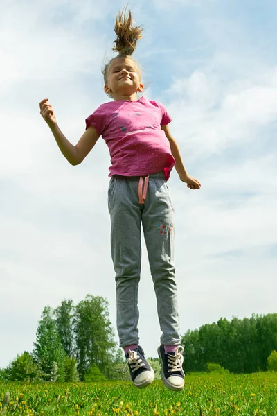 Kleines Mädchen springt und spielt auf einer grünen Wiese im Park. Sommerkonzept, Kinderspiele an der frischen Luft. lizenzfreie Stockfotos