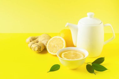 Zencefil limon çayı veya detoks beyaz bir fincan ve parlak sarı bir arka plan üzerinde bir çaydanlık içinde içki. Sağlıklı beslenme konsepti.