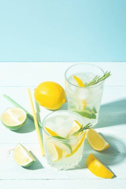 Parlak güneş ışığı ile mavi bir arka plan üzerinde zarif bir bardak limon ve limon bir içki. Yaz kokteyli veya mojito.