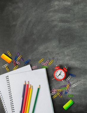 Tebeşir tahtasının arka planında eğitim malzemeleri defter kalem kalemleri çalar saat. Kavram okula geri.