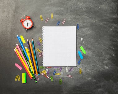 Tebeşir tahtasının arka planında eğitim malzemeleri defter kalem kalemleri çalar saat. Kavram okula geri.