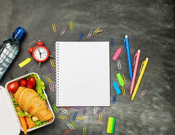 Sandwich bottle of water teaching supplies notebook pen on a chalk board. Concept back to school. Top view flat layout.