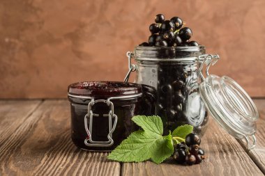 Cam kavanozlarda reçel ve taze siyah frenk üzümü meyveleri ahşap bir arka planda durmak. Yatay çerçeve. Seçici odak.
