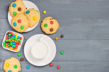 Gri arka planda renkli jöle fasulye şekerleri ile süslenmiş süt ve ev yapımı kurabiye bir fincan. Üst görünüm düz düzen