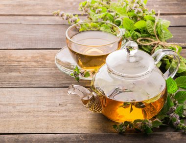 Ahşap rustik bir arka plan üzerinde bir fincan ve çaydanlık limon balsam nane taze yaprakları ile Çay. Şifa bitkisel içecek.