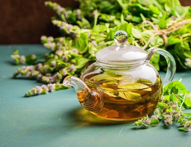 Melissa nane ile taze aromatik çay rustik bir arka plan üzerinde cam çaydanlık bırakır. Şifalı bitkisel içecek. Yatay çerçeve.