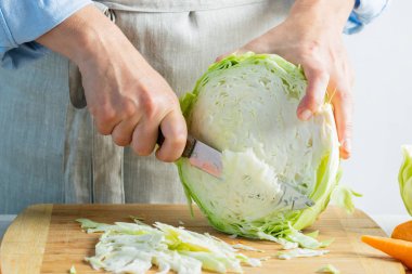 Woman slices fresh organic cabbage for making salad or for salting cabbage natural background. Vegetarian food concept. clipart
