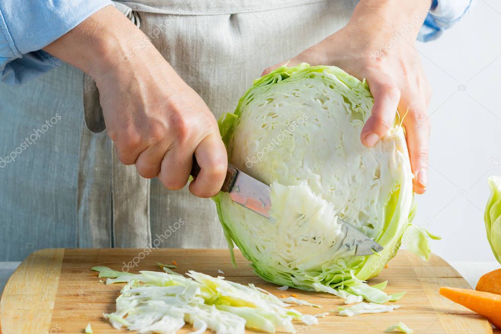 Woman slices fresh organic cabbage for making salad or for salting cabbage natural background. Vegetarian food concept.