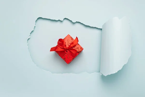 Gift with a red bow on the background of a big hole on a paper background mint color. Holiday concept. Flat layout.