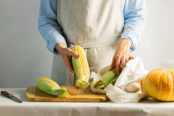 Bir kadın aşçı pamuk önlük koçan üzerinde olgun mısır temizler. Rustik doğal stil. Organik gıda kavramı. Kinfolk tarzı. — Stok fotoğraf