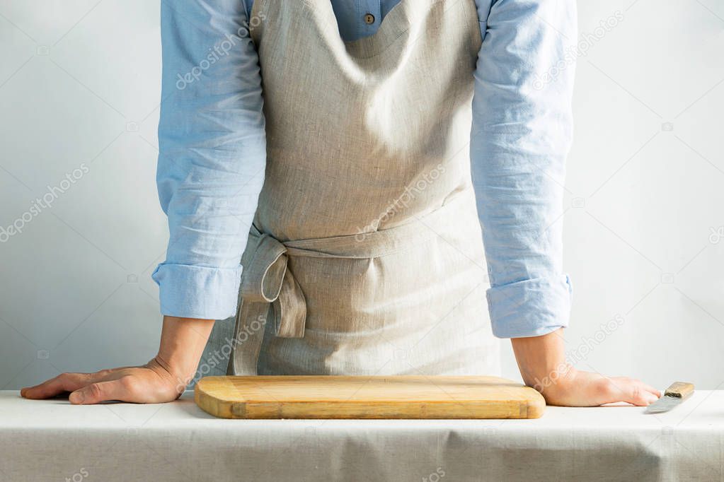 Female cook in cotton apron at the kitchen table with cutting board. Rustic natural style. Kinfolk concept. Copy space.