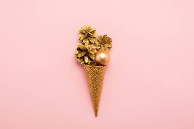Dondurma waffle fincan konileri Noel topları bir pastel pembe arka plan üzerinde altın boyalı. Yeni Yıl veya Noel konsepti.
