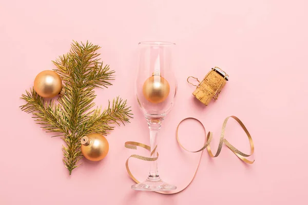 New Year or Christmas layout balls glass goblet branch spruce serpentine cork from bottle of gold color pink background.