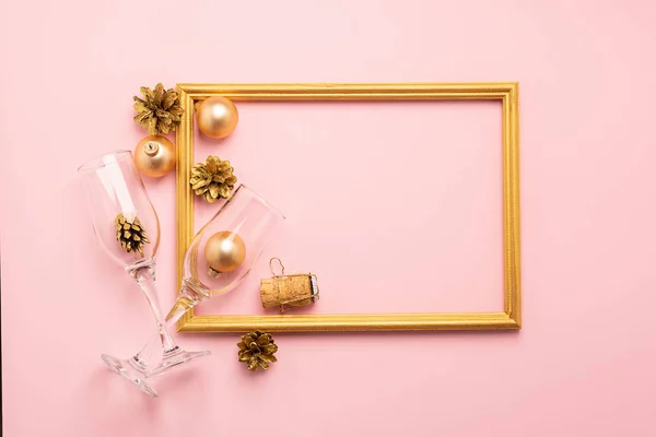 New Year or Christmas layout balls serpentine cork from a bottle of gold color empty wine glasses on a pink background.
