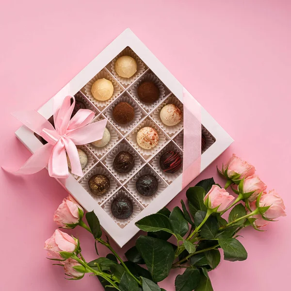 Chocolates from various Belgian chocolate in a festive box on a pink background a bouquet roses. Exclusive dessert gift.